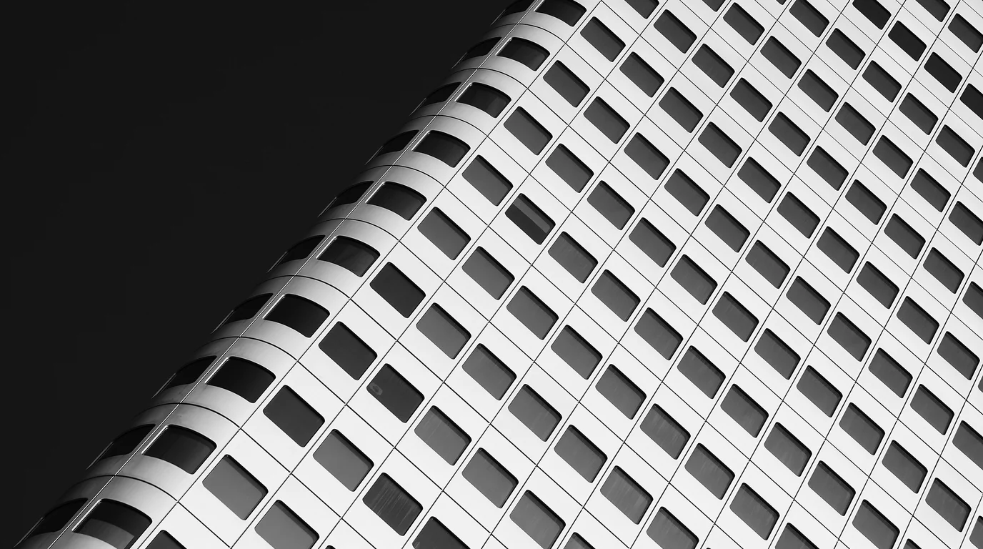 Black-and-white close-up of a rounded office tower's facade, rows of square windows curving away against a dark sky.