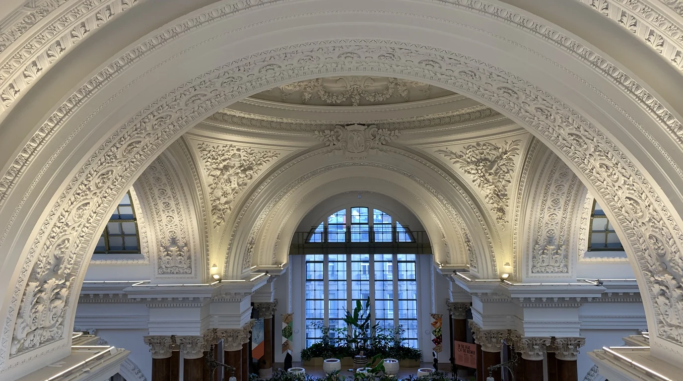 A sculpted white plaster arch framing a tall arched window inside the former Brussels Stock Exchange.