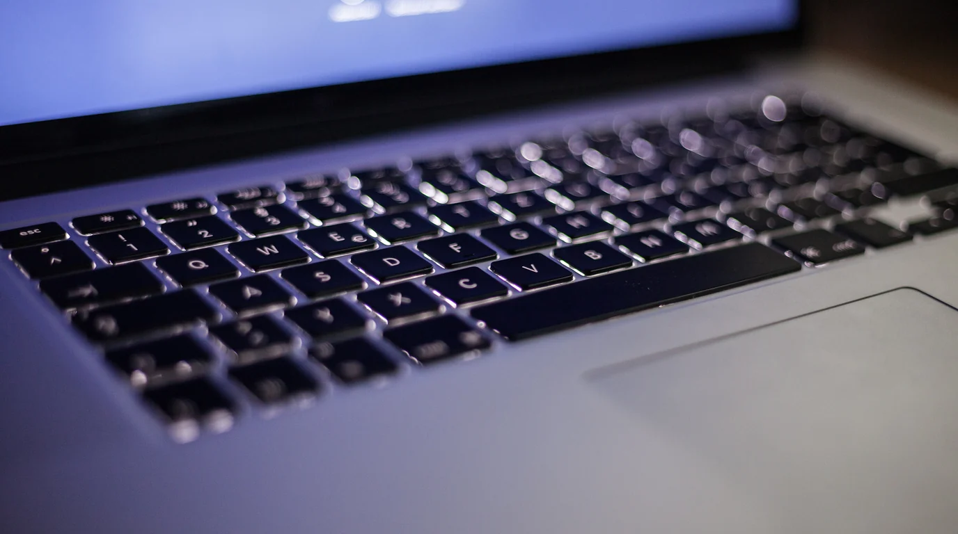 Close-up of a laptop's backlit keyboard in cool blue light.