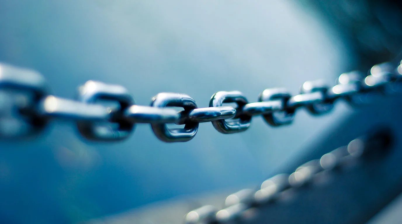 A steel chain stretched across the frame, its links in sharp focus against a blurred blue background.