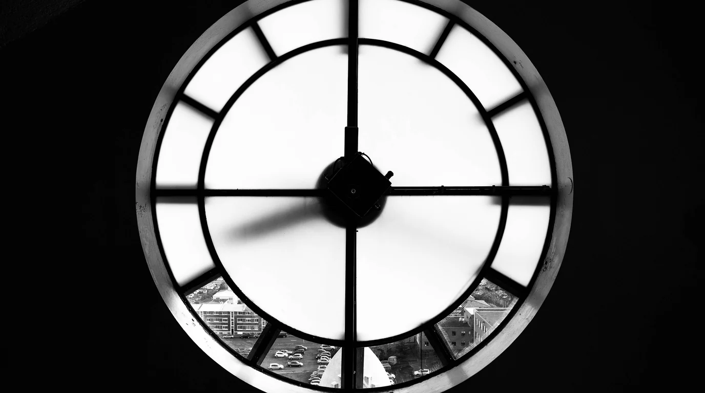 A tower clock face seen from inside, its black hands and frame silhouetted against the bright glass.