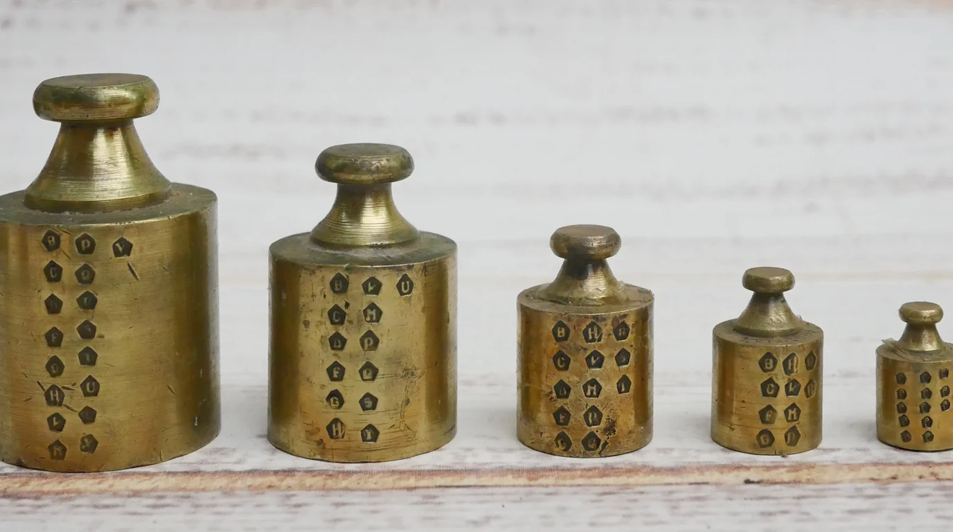 A row of old brass weights stamped with marks, lined up from largest to smallest.