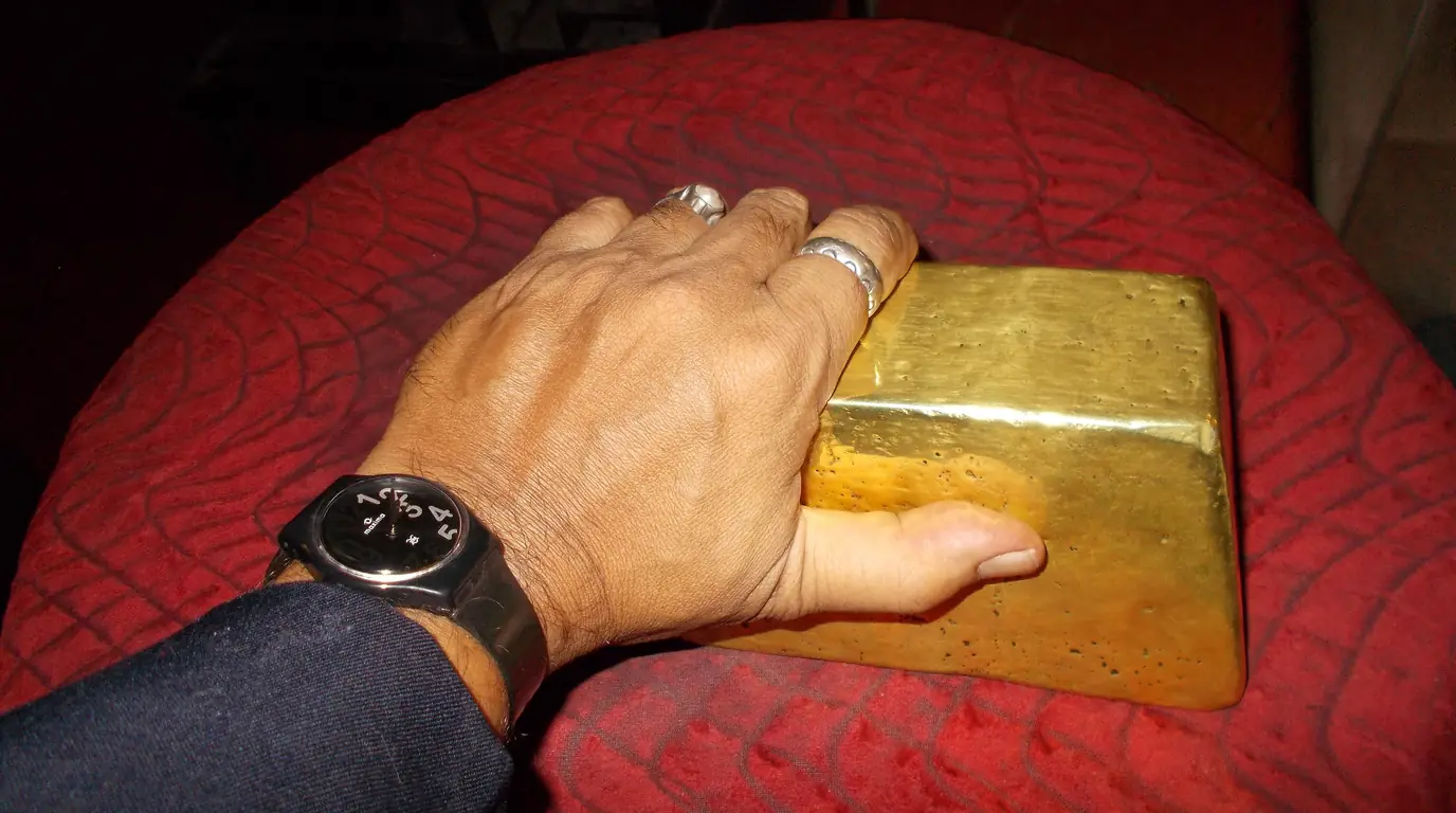 A hand resting on a large, heavy gold ingot placed on a red cushion.