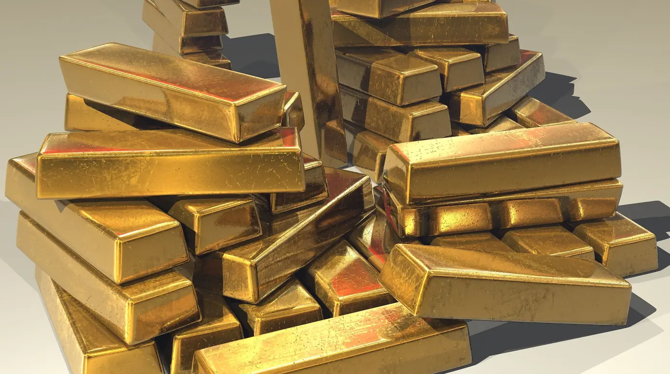 Gold bullion bars stacked in an untidy pile on a pale surface, lit from the side.