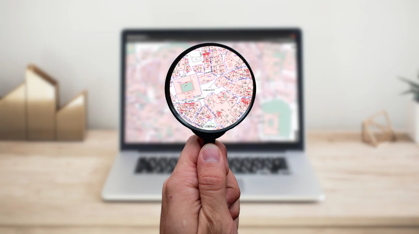 A hand holding a magnifying glass over a map shown on a laptop screen.