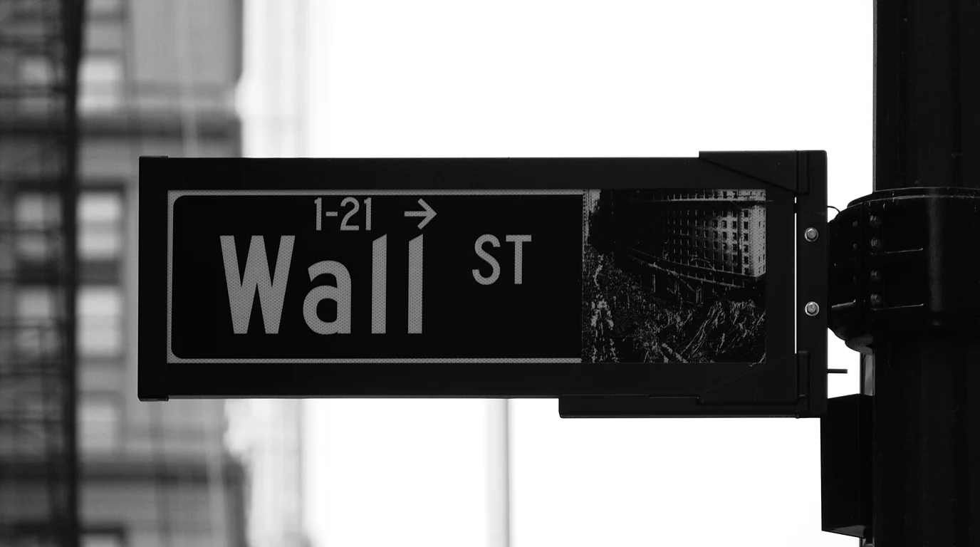 A black Wall St street sign mounted on a pole against a pale sky.