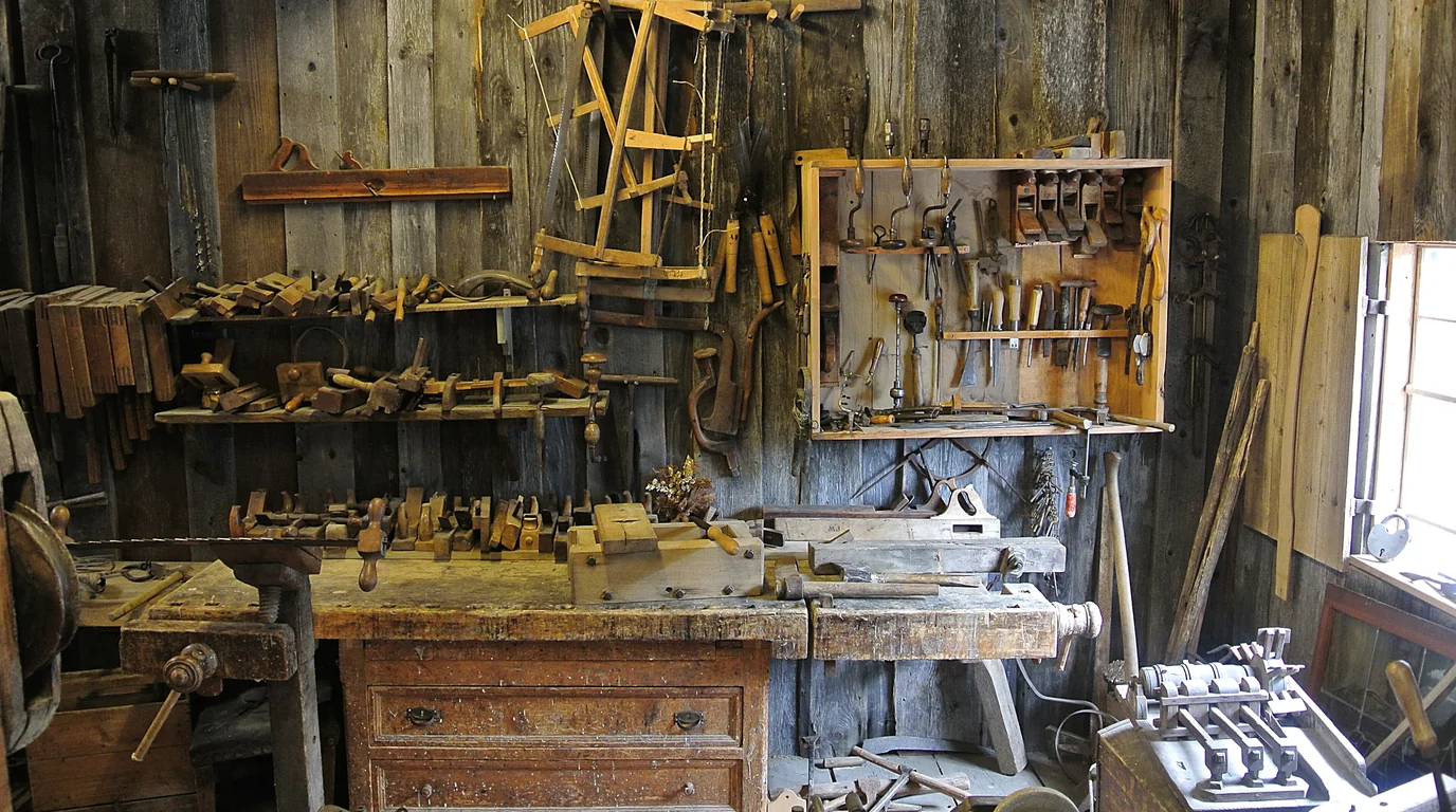 An old woodworking workshop with hand planes, saws and clamps hung on the walls above a workbench.