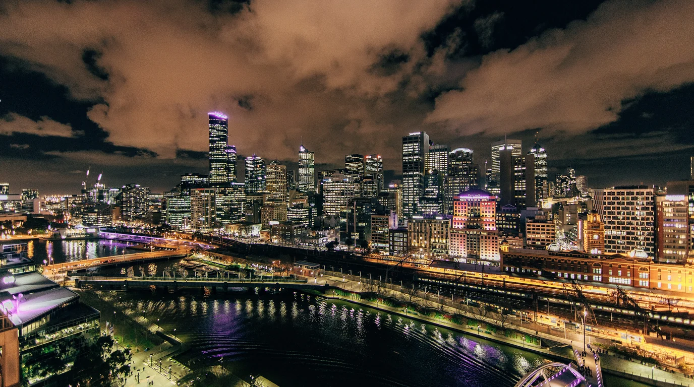 Melbourne's city skyline and the Yarra River lit up at night under heavy cloud.