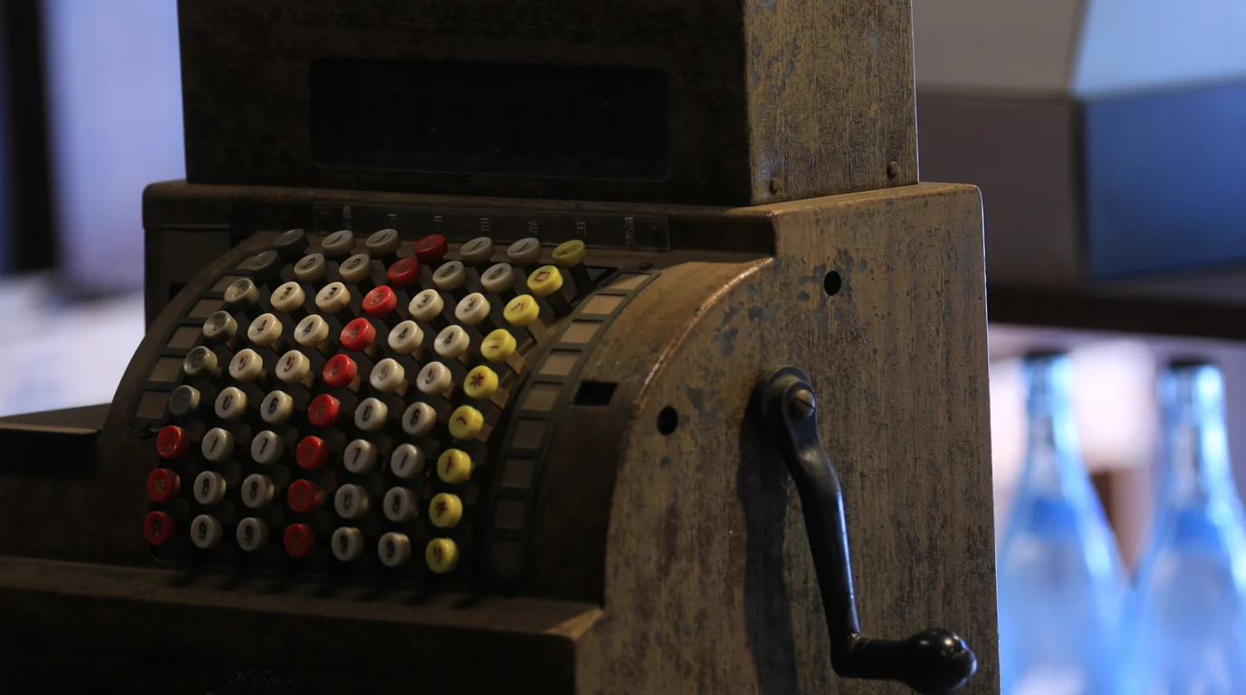 An old mechanical cash register with rows of coloured round keys and a side crank.