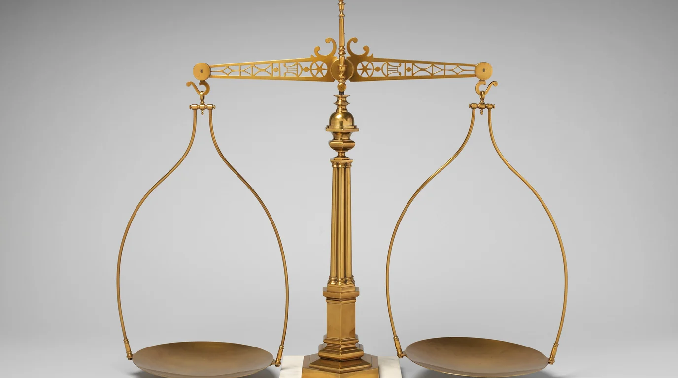 A tall gilded balance scale with two empty pans, on a light grey background.