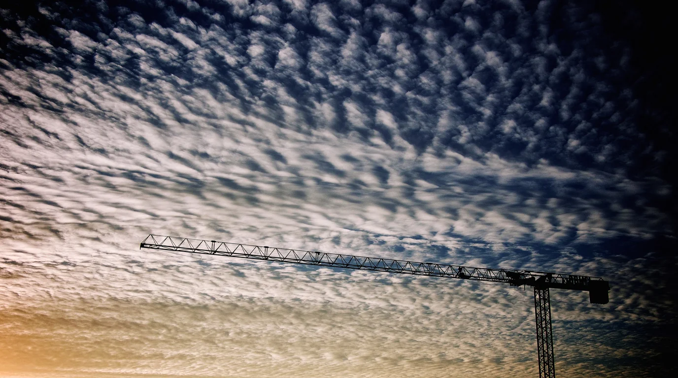 A tower crane's long jib silhouetted against a sky of rippled clouds.